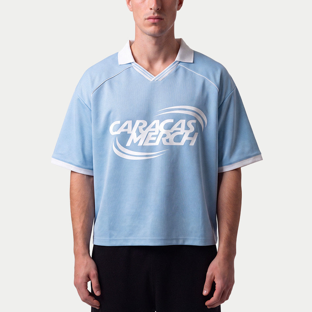 Hombre llevando la camiseta de fútbol boxy azul claro de Caracas Merch con cuello blanco